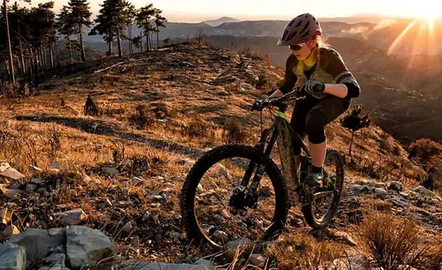 Une femme sur un vélo à assistance électrique en montagne au couché de soleil en fond
